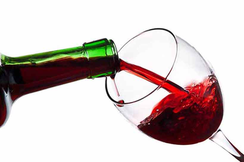 Verter una copa de vino tinto de una botella verde.