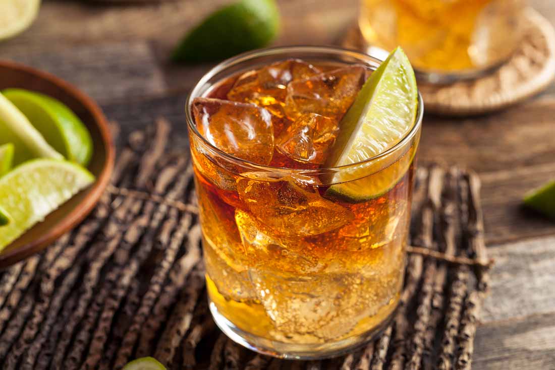 Vaso de ron con cubitos de hielo y rodaja de limón.