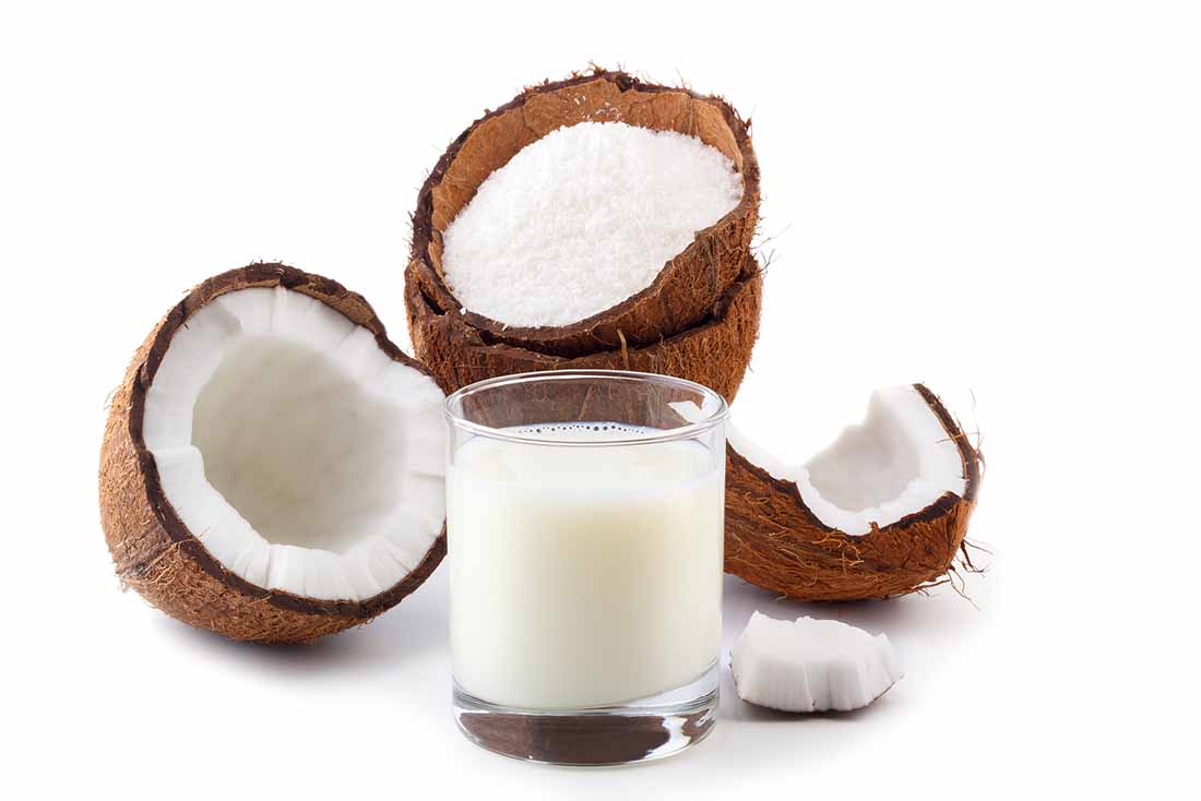 Vaso de leche de coco junto a la mitad - Coco roto.