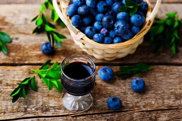 Copa de vino azul junto a la cesta de arándanos.