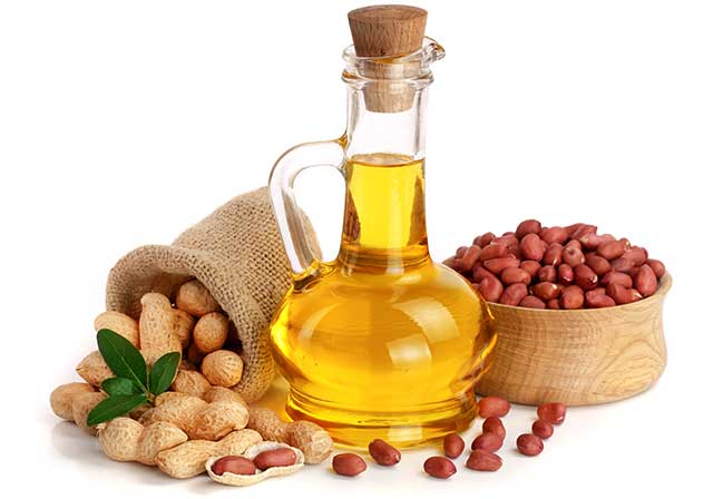 Aceite de maní en una botella de vidrio junto a un tazón de maní.